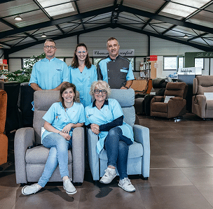 Cinq professionnels souriants en uniforme. Deux femmes en sièges confort dans showroom. Panneau 'Chaussons Confort'.