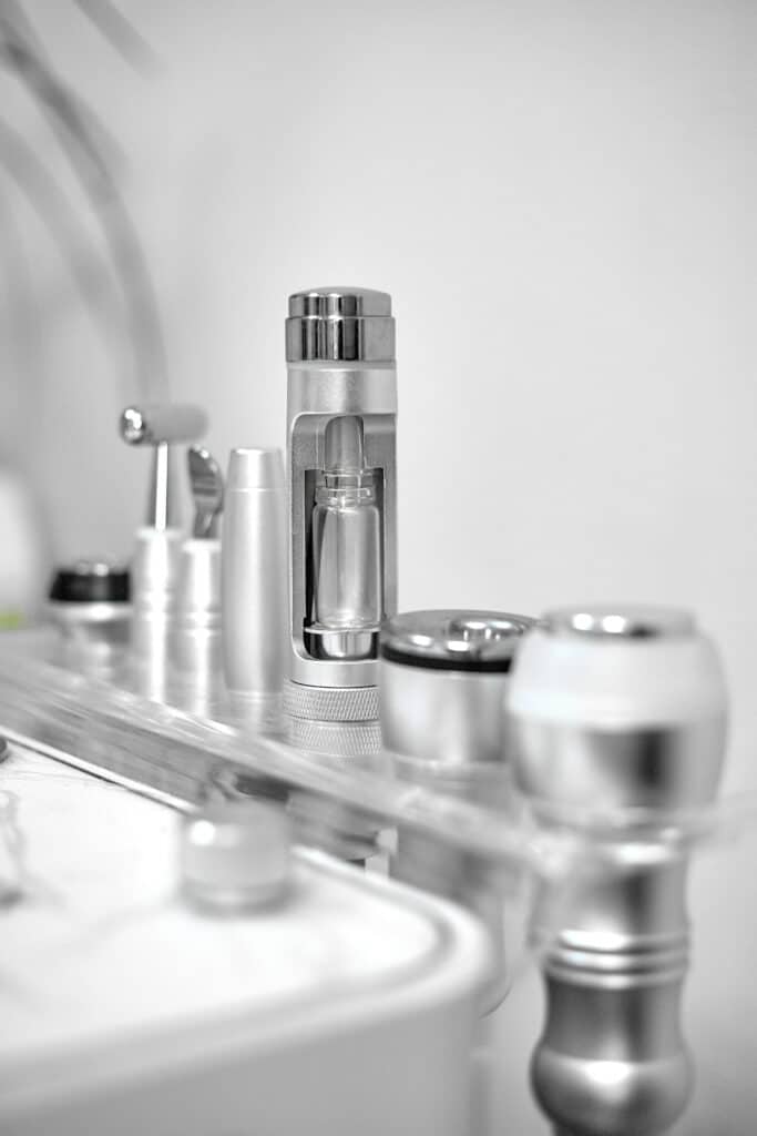 Gros plan d'équipement de laboratoire stérile : instrument cylindrique métallique avec flacon en verre, sur surface réfléchissante.